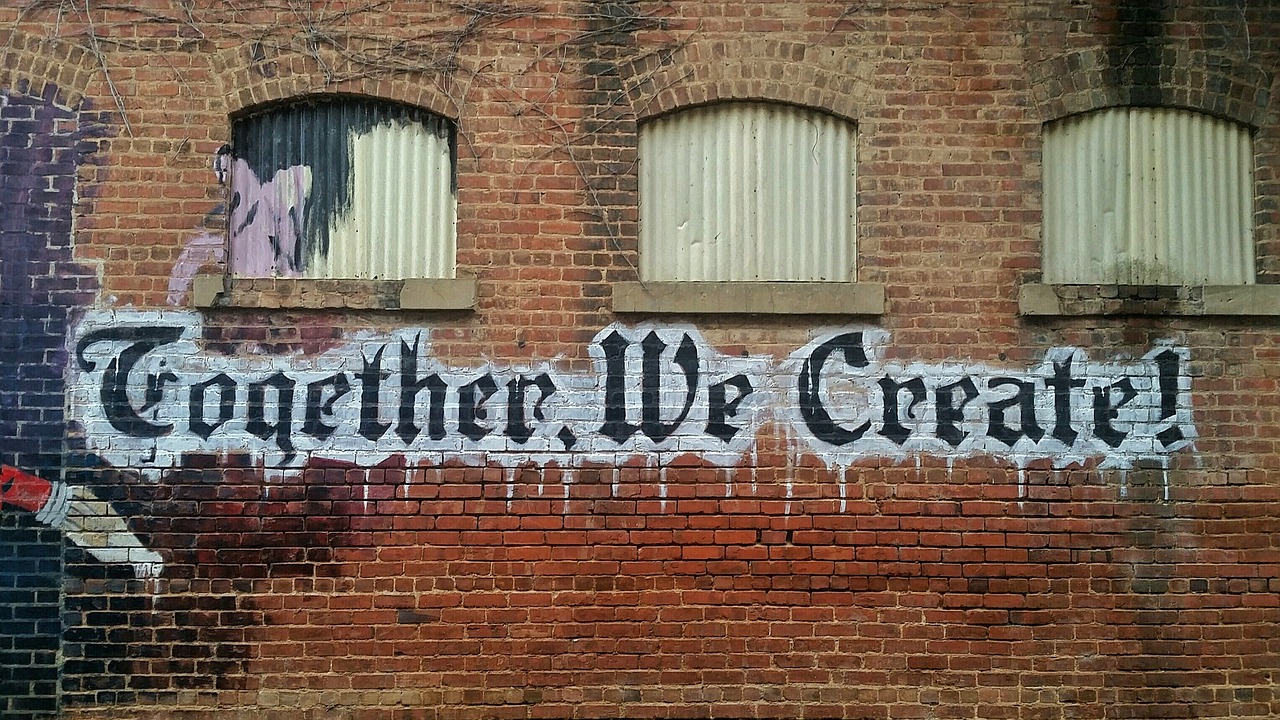 Graffiti in a gothic style on a brick wall that reads "Together, we create!"